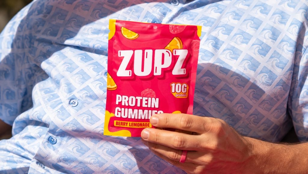 Zupz protein gummy packaging by BeMain Studio featuring a Berry Lemonade pouch held in hand with bold pink and yellow branding.